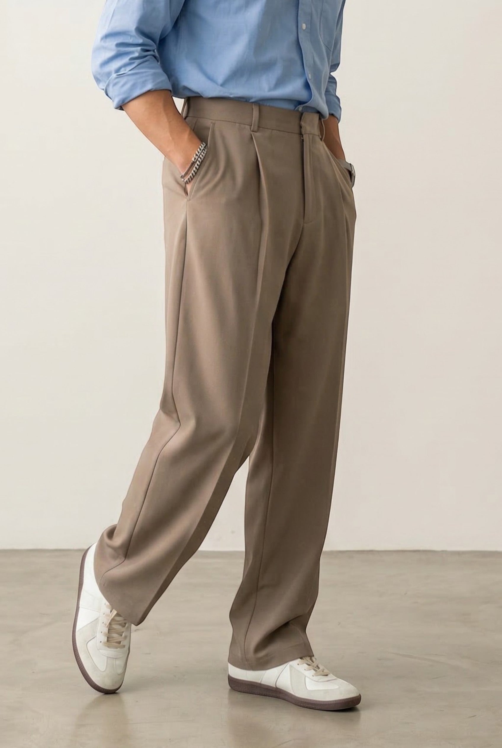 Tuck It taupe pleated trousers with a relaxed fit and side pockets, paired with a blue button-up shirt.